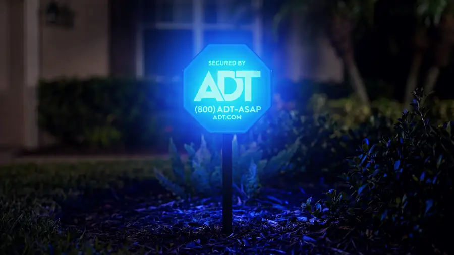 Illuminated Secured by ADT yard sign in the front garden of a home at night